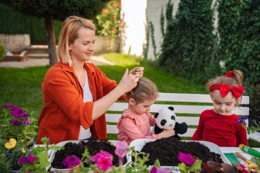 Bir anne çiçek dikerken kızının saçını şekillendirir..