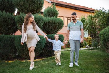 Hamile çift, genç oğullarıyla el ele yürür..