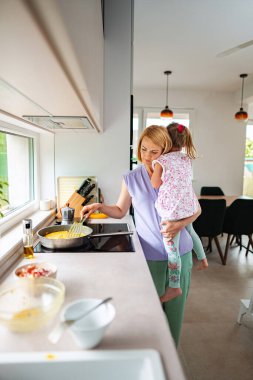 Anne kızını yanında tutarken kahvaltı hazırlar..