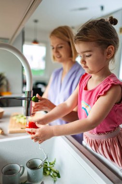 Çocuk mutfakta sebzeleri neşeyle yıkıyor..