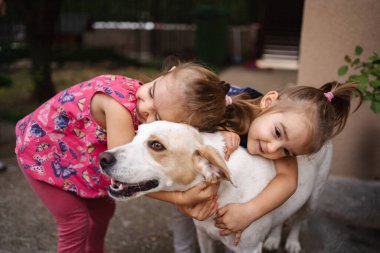 İki genç kız kardeş mutlu bir şekilde evlerinde dost canlısı köpeklerine sarılıyorlar..