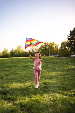 Genç bir kız neşeyle yemyeşil bir tarlada koşuyor, kafasının üstünde canlı bir gökkuşağı uçurtması tutuyor. Güneş arka planda yavaşça batar, sahne üzerine sıcak bir parıltı yayar..