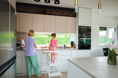 Bir yetişkin yemek hazırlarken bir çocuk mutfakta yardım eder..