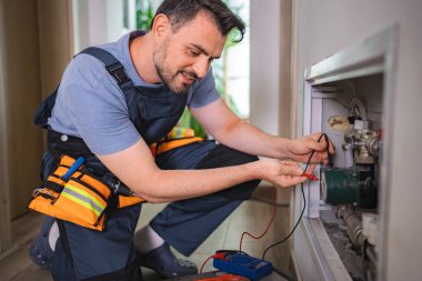 Teknisyen ısıtma sistemi borularında çoklu metre kullanarak voltajı kontrol ediyor