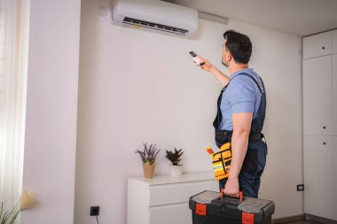 HVAC teknisyeni havalandırma ünitesini test etmek için uzaktan kumanda kullanıyor.