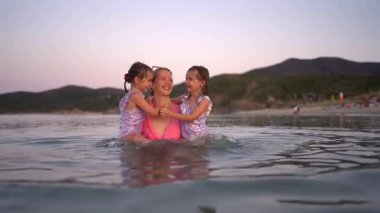 Anne ve iki kızı gün batımında sakin denizde rahatlatıcı bir banyo yapıyorlar.