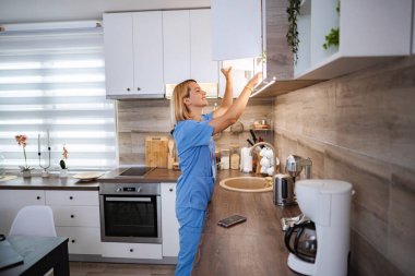 Ev ziyareti sırasında hastalarının mutfağında mola veren gülümseyen kadın doktor.