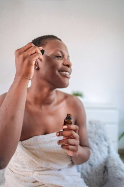 Gülümseyen genç siyah kadın duş aldıktan sonra yüzüne gerekli yağı sürüyor.