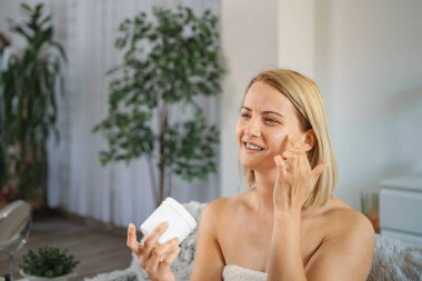 Gülümseyen kadın yüzüne nemlendirici krem sürüyor.