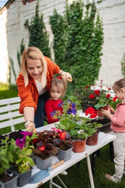 Bir kadın çocuklara birlikte çiçek dikmeyi öğretiyor..