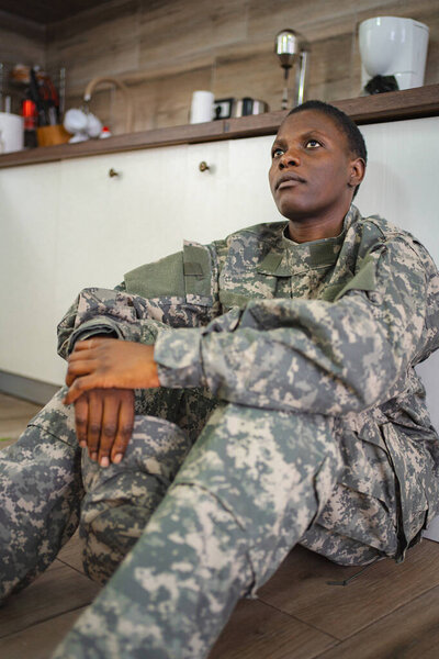 American soldier in camouflage uniform sitting on the floor, appearing pensive and thoughtful