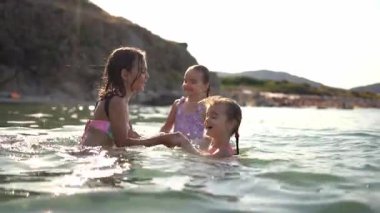 Üç kız sahile yakın denizde su sıçratırken eğleniyor.