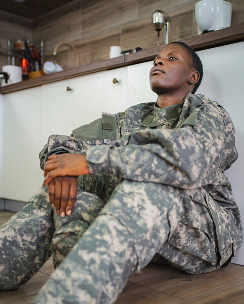 Depressed african american soldier sitting on the kitchen floor, suffering from post-traumatic stress disorder