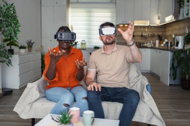 Kanepede oturup sanal gerçekliği keşfeden genç çift.