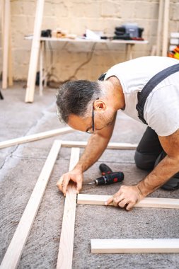 Olgun erkek marangoz, tahtadan bir tahta üzerinde elektrikli tornavida kullanıyor..