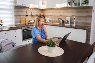 Uzun bir vardiyadan sonra dizüstü bilgisayarı üzerinde çalışırken esnemekten yorgun düşmüş kadın doktor.