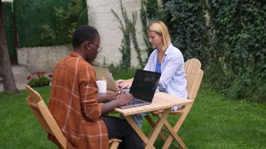 Bahçede dizüstü bilgisayarlarıyla çalışan iki genç girişimci.