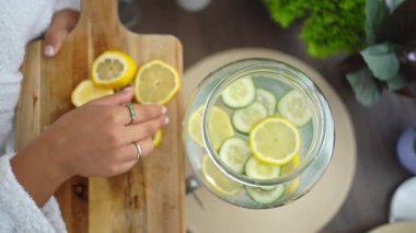 Salatalık ve su dolu cam kavanoza limon dilimleri ekleyen bir kadın.