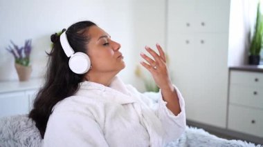 Bornoz giyen, kulaklıkla müzik dinleyen ve ellerini hareket ettiren genç bir kadın.