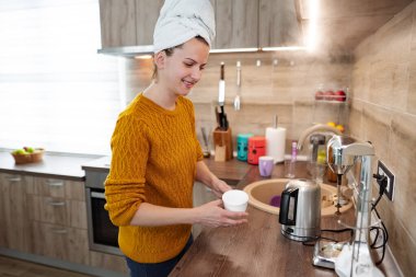 Kafasında bir havluyla mutfakta duran bir kadın var. Kendine kahve yapıyor..