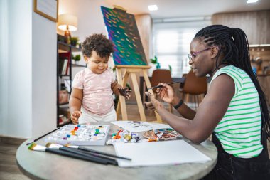 Neşeli bir anne renkli bir resim aktivitesinde çocuğuna rehberlik eder..