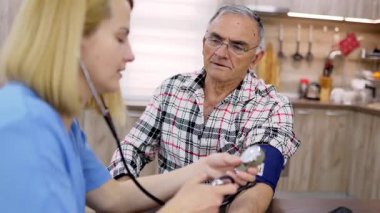 Hemşire evde yaşlı bir adamın tansiyonunu ölçüyor.