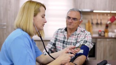 Hemşire evdeki yaşlı adamın kan basıncını ölçüyor.
