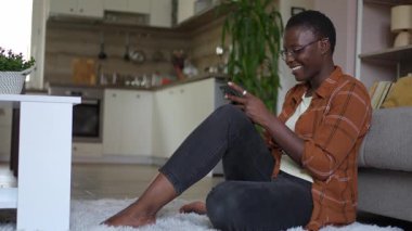 Evde akıllı telefon kullanan genç bir kadın yerde oturuyor.