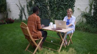 İki iş arkadaşı bir bahçede dizüstü bilgisayarlarıyla çalışıyor.
