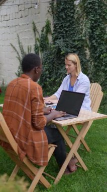 İki iş arkadaşı bir bahçede dizüstü bilgisayarlarıyla çalışıyor.