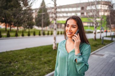 Genç bir kadın parkta yürürken bir telefon görüşmesi yapıyor.
