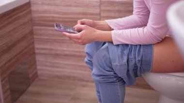 Tuvalette otururken cep telefonu kullanan bir kadın.