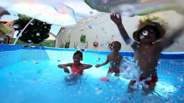 Mutlu çocuklar yazın arka bahçedeki yüzme havuzunda eğleniyor ve su sıçratıyor.