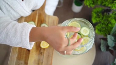 Güzellik uzmanı bir kavanoz detoks suyuna salatalık ve limon dilimleri ekliyor.