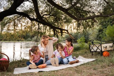 Anne, ormanda nehir kenarında piknik yaparken üç kızıyla eğleniyor.
