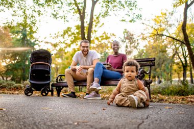 Canlı bir park kurmak bir aileyi birlikte eğlenirken yakalar. Bir bebek yerde oynarken, ebeveynler sonbahar yapraklarıyla çevrili bir bankta neşeli anları paylaşıyorlar..