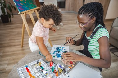 A mother and her young child paint together, sharing joyful creativity.
