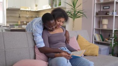 Two young African American women enjoy quality time together, reading a book on a comfortable sofa in their living room