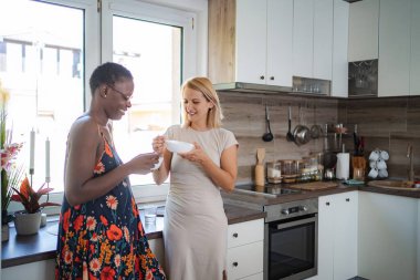 Two diverse women are sharing a moment together, eating breakfast in a bright, modern kitchen