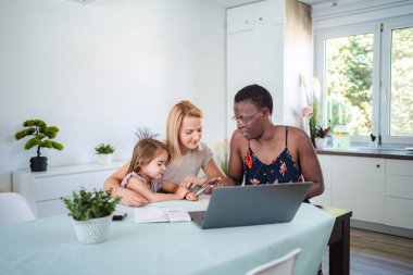 Mother and daughter studying with a home tutor using a laptop in their kitchen