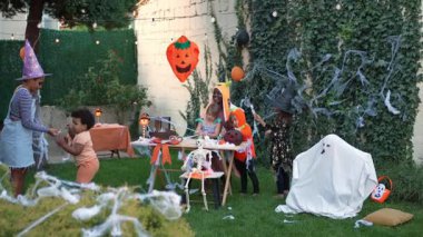 Funny child in a ghost costume scaring his friends during a Halloween party in the backyard