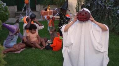 Ghost with a pumpkin head scaring a group of children at a halloween party in the garden