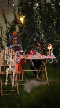 Two girls in witch costumes playing with a jack-o-lantern during a Halloween party at night