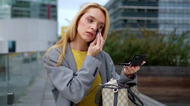 Fashionable woman refreshing her makeup with powder and a pocket mirror on a city street