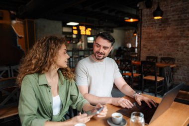 İki genç girişimci bir kafede dizüstü bilgisayarda bir projeyi tartışıyor, kahve molasının keyfini çıkarıyorlar.