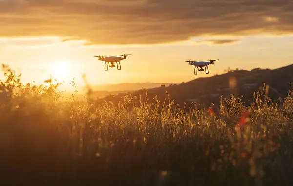 Bir DJI Mavic Hava Aracı gökyüzünde uçuyor, arkasında da bir başkası, her ikisi de gün batımında açık bir arazide uçuyor. Üretici yapay zeka.