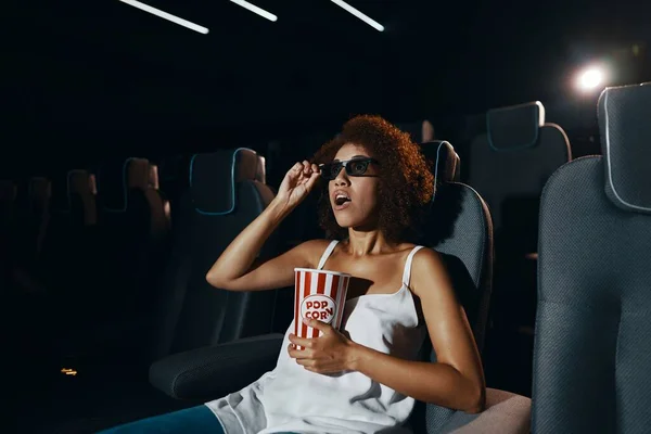 A young woman in 3D glasses is watching a movie enthusiastically. Popcorn in hands. High quality photo