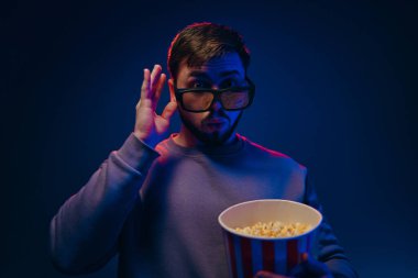 Bir adam karanlık bir odada neon ışıklı, 3D gözlüklü ve patlamış mısırlı bir film izliyor. Yüksek kalite fotoğraf