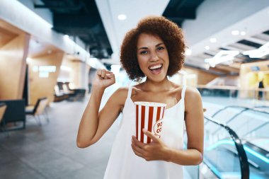 Beyaz gömlekli kıvırcık saçlı kadın elinde patlamış mısırla film izlemek için yürüyor. Yüksek kalite fotoğraf
