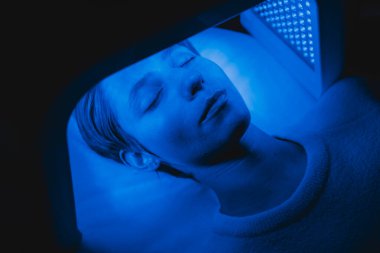 Genç bir kadın LED ışığının yardımıyla yüzünün derisini tedavi ediyor. Yüksek kalite fotoğraf